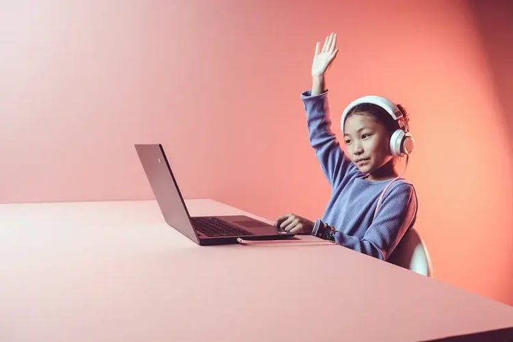 Newport-Mesa 6th grader at a Chromebook with headphones, raising hand during a Soundtrap class